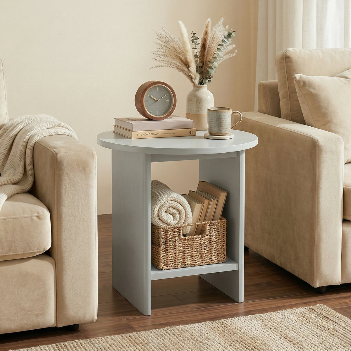 [Grey] Small Round Side Table with Shelf Living Room positioned between two cream sofas with clock and botanical vase on top and wicker basket on lower shelf