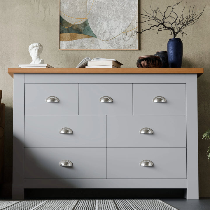 [Grey] Shaker 7 drawer wide chest with oak top cup handles and abstract art on textured wall.