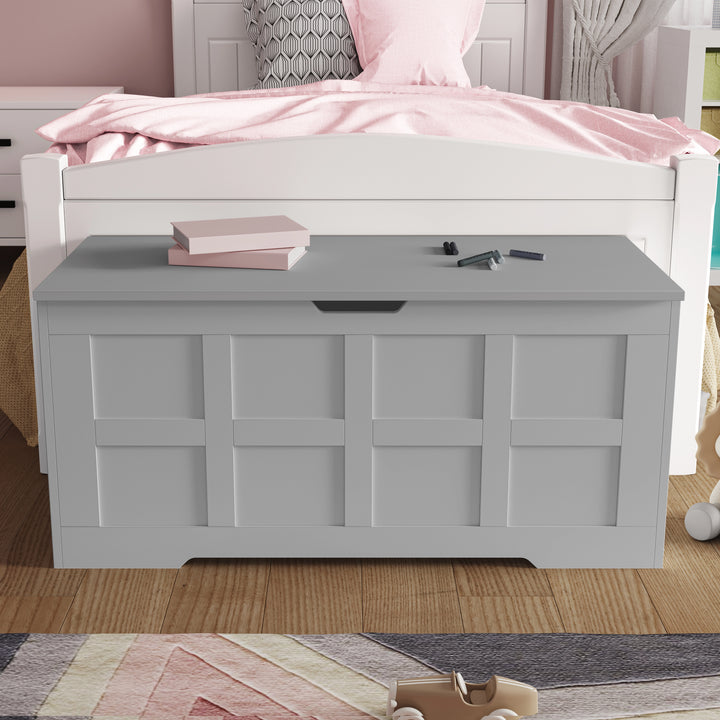 [Grey] Side-angle view of closed grey shaker storage chest with cutout side handle, pink book on top and striped rug below