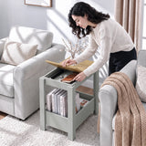 [Grey] A woman lifts a tabletop panel and reaches into the storage compartment beside a sofa, with books below.