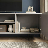 [Grey] Open-door view of grey TV unit, internal compartments holding books and home accessories, dark navy wall behind.