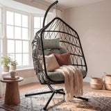 [Black] Black hanging egg chair beside round wooden side table with potted plant and woven baskets in cream painted room