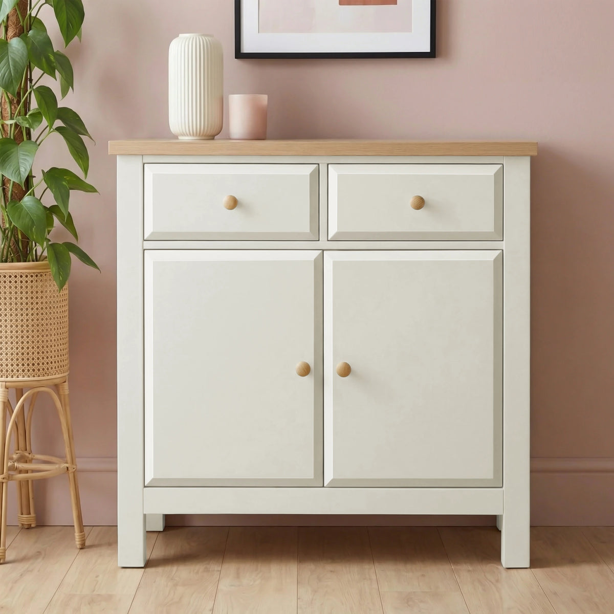 [White]  2 door sideboard cabinet with wooden top against a pink wall with decorative items