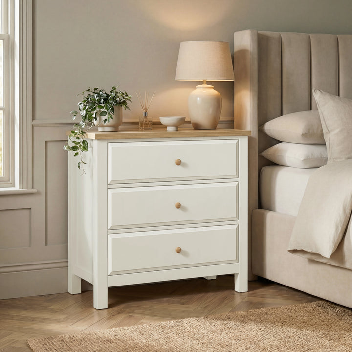 [White] Haven 3-drawer chest in a bedroom setting with lamp on oak top and upholstered headboard panel behind