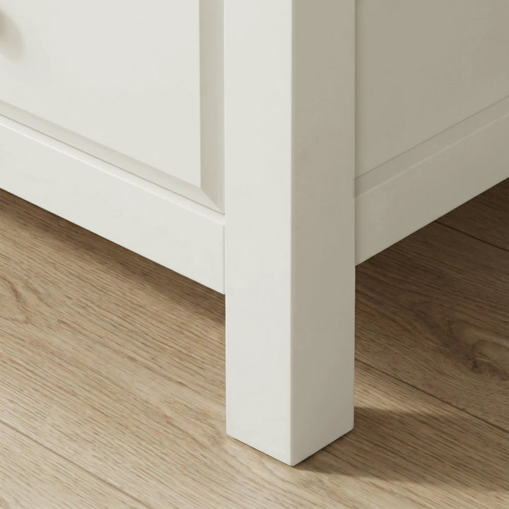 [White] Haven 5-drawer tall chest angled close-up showing painted frame leg and base detail against wooden floor