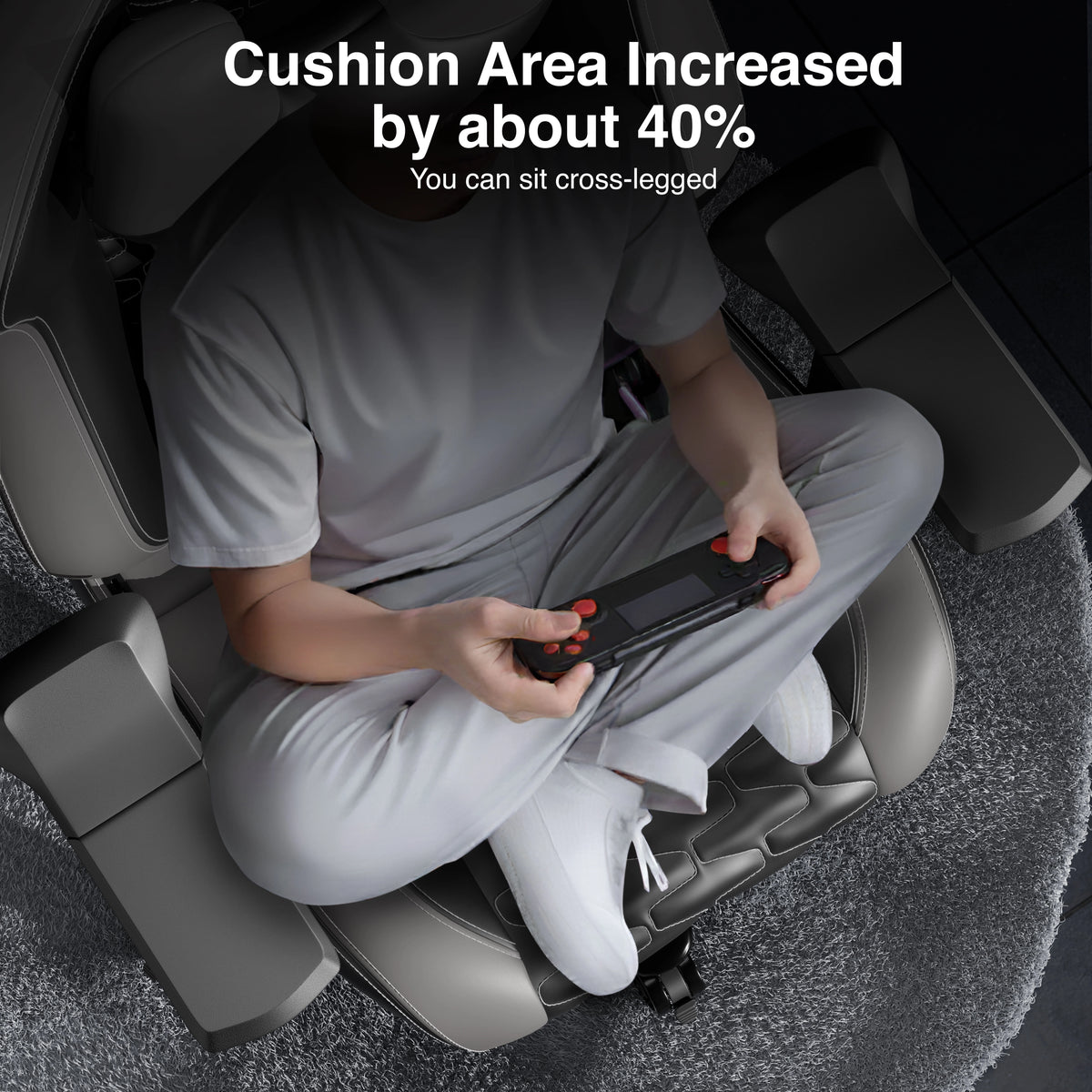 [Black + Grey] Person sitting on a massage chair with increased cushion area, holding a remote control.