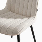 [Vertical Beige | Clear] Close-up of Kyvon beige upholstered fabric channeled stitched chair seat with black metal legs