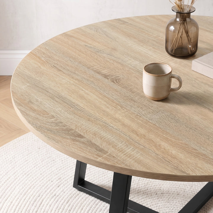 [Pink | Sonoma Oak] Close-up of Kyvon round dining table set's sonoma oak-effect tabletop and black base