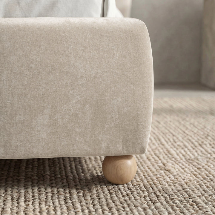 [Beige | King] Round wooden ball foot at base corner sitting on woven jute rug with upholstered frame edge visible above