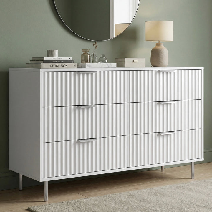 [White] dresser with metallic handles in a room with a green wall and round mirror