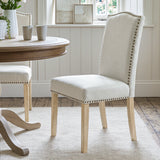 [Beige | Set of 2] Nailhead dining chair beside a round wooden table in a bright dining room
