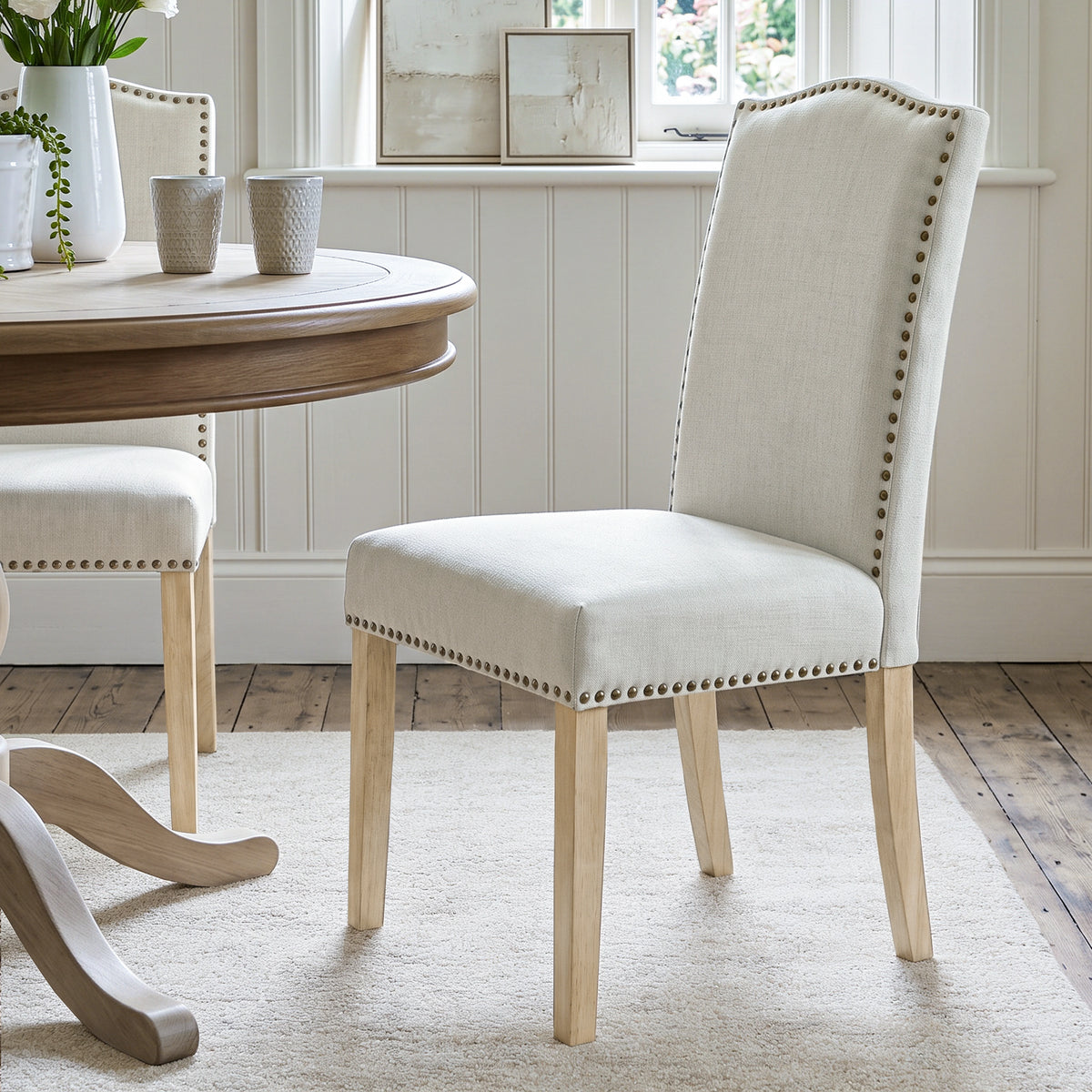 [Beige | Set of 2] Nailhead dining chair beside a round wooden table in a bright dining room