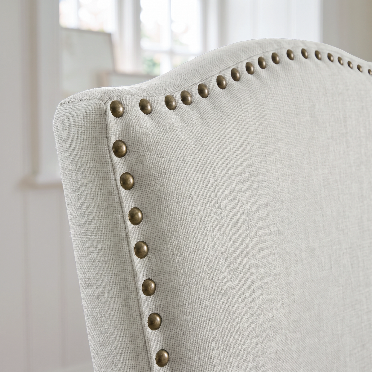 [Beige | Set of 4] Close-up of curved high back with fabric upholstery and bronze nailhead trim