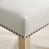 [Beige | Set of 4] Close-up of fabric seat, bronze nailhead trim and light wooden leg on the dining chair