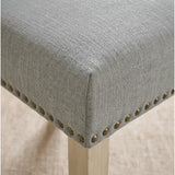 [Light Grey | Set of 2] Close-up of fabric seat, bronze nailhead trim and light wooden leg on the dining chair