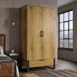 [Oak Effect] Rustvale wardrobe angled view with closed double doors, lower drawer, black handles, concrete wall, and window.