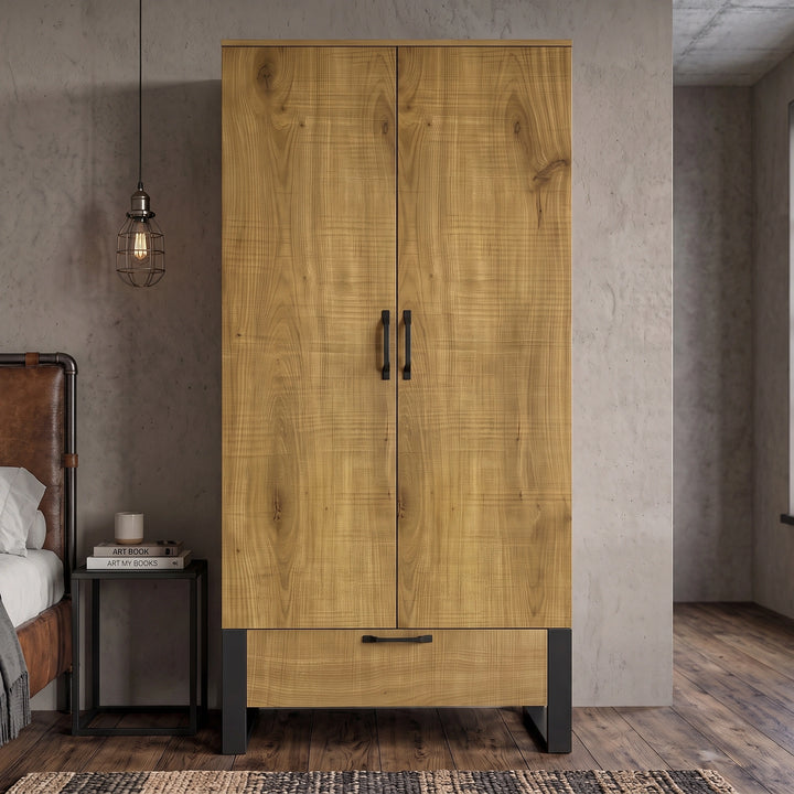 [Oak Effect] Rustvale wardrobe front view with closed double doors, lower drawer, black metal legs, concrete wall, and stool.