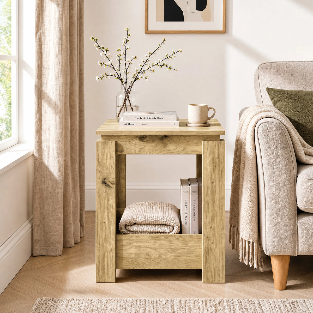 [Oak] Front view of the square side table beside a sofa, with books and a folded throw stored below