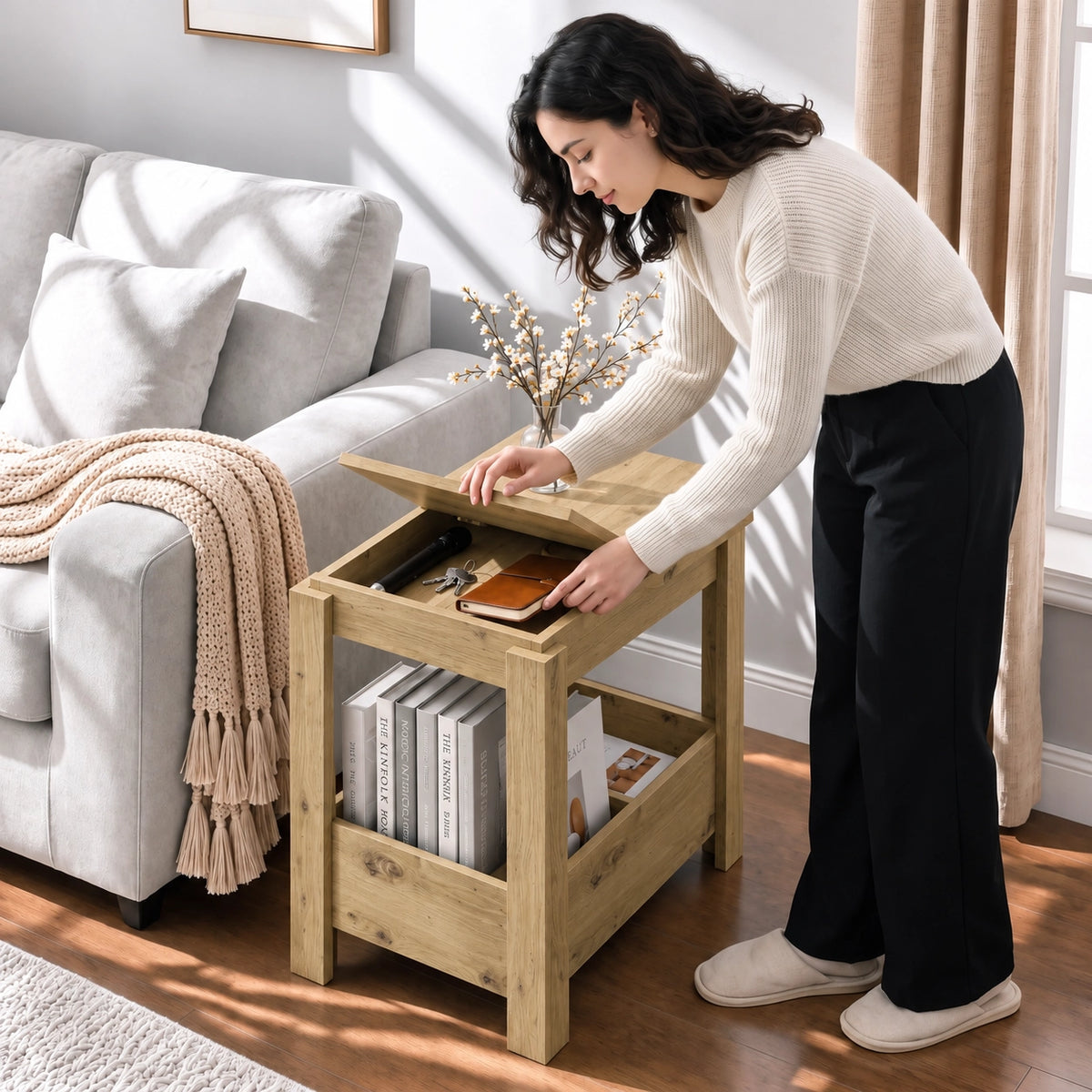 [Oak] A woman reaches into the open top storage beside a sofa, with a blossom vase and books visible on the side table.