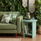 [Sage Green] Round sage green end table styled in plant-filled lounge with glass terrarium and books on shelf