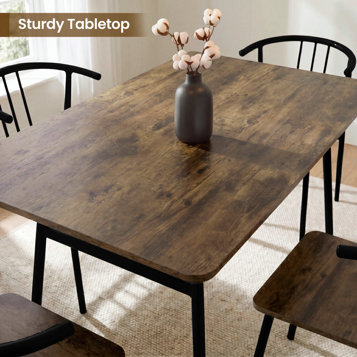 [Rustic] Torvi dining table overhead close-up showing dark rustic wood-effect tabletop surface with a cotton stem vase and black metal arm chairs around it