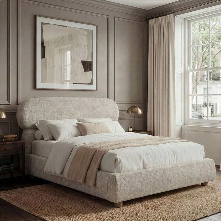 [Double | Camel] Woven fabric bed from the side with rounded capsule headboard and layered neutral bedding
