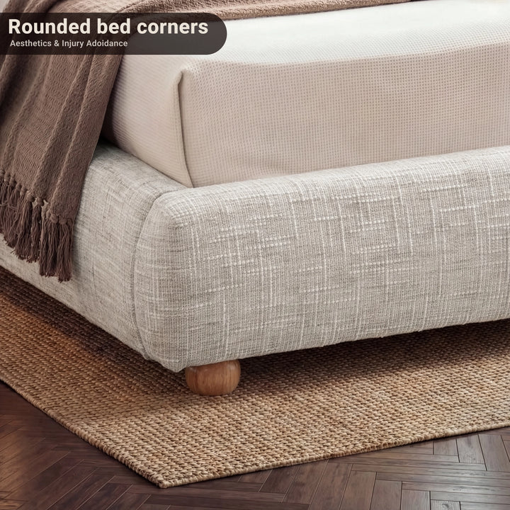[King | Camel] Close-up of bed frame corner showing rounded padded base with wooden ball foot on textured rug