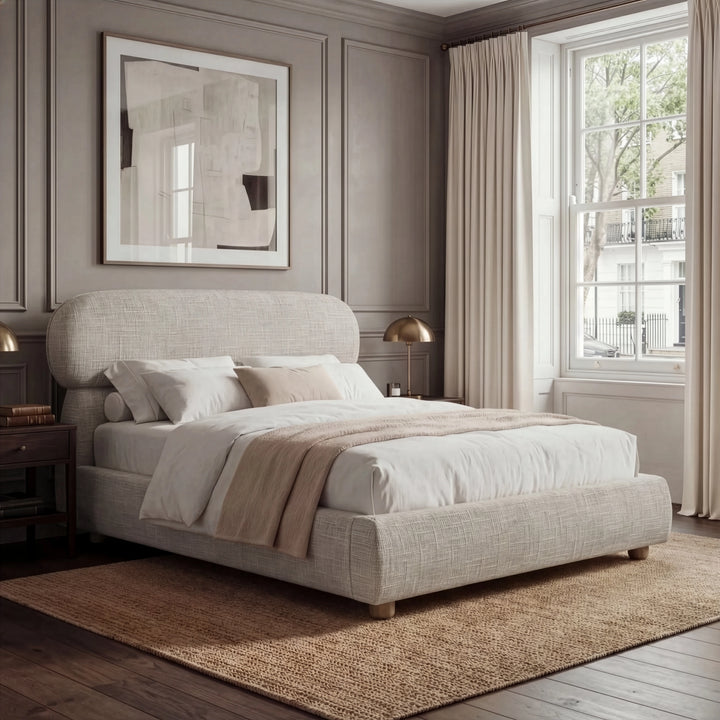 [King | Camel] Fabric bed with luxury rounded headboard beside nightstand with table lamp and natural daylight