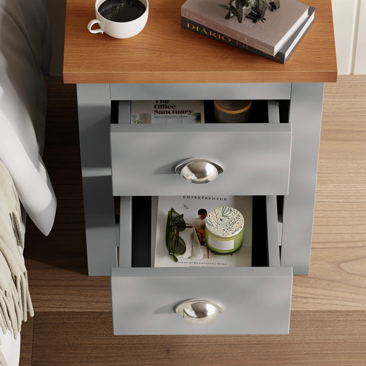 [Grey] Open drawers of grey 2 drawer bedside table showing interior storage with books and candles, placed next to a bed.