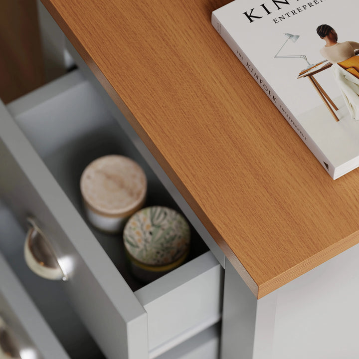[Grey] Close-up of oak-look top and open drawer of grey bedside table showing interior with candles and a book on top.