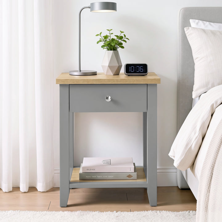 [Grey] Bedside lifestyle view with lamp, plant and clock on top, closed drawer and lower shelf