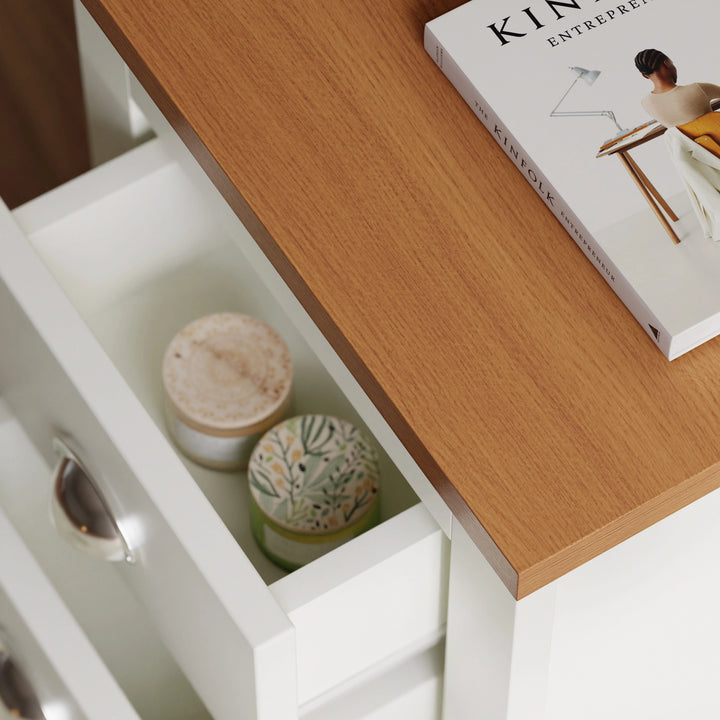[White] Close-up of oak-look top and open drawer of white bedside table showing interior storage with candles and book.
