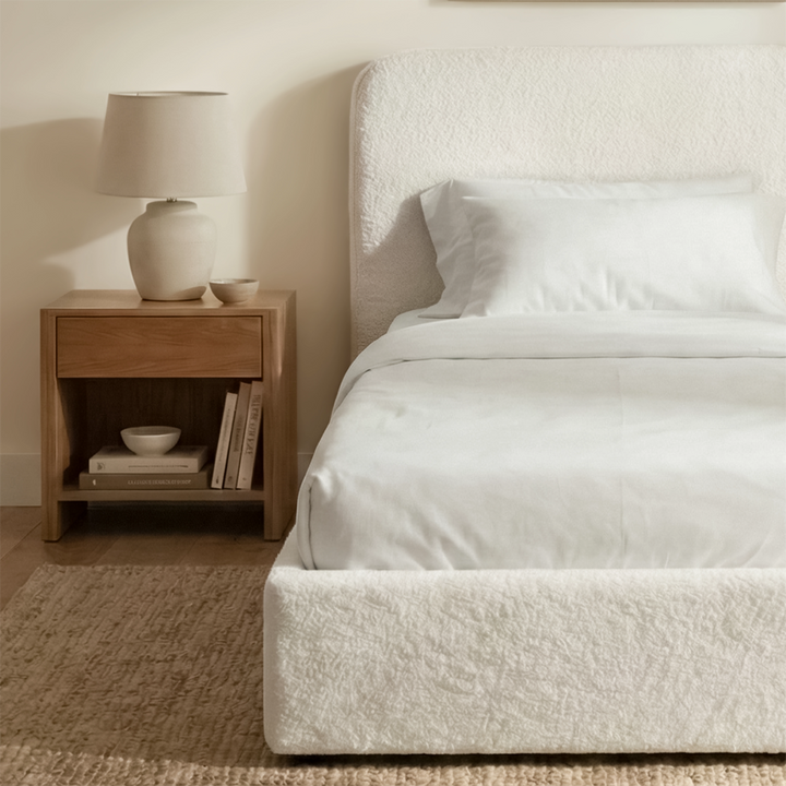 [White | Single] Sofna boucle ottoman bed from the side, white boucle side rail and puffed headboard beside a wooden bedside