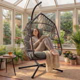 [Grey] Grey rattan egg chair with seated woman in glass-walled garden room next to wooden side table