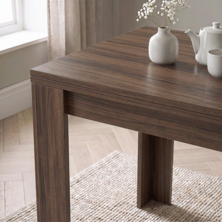 [Walnut] Close-up of folded wood-grain square tabletop above apron and wide legs, with flower vase, teapot and cup