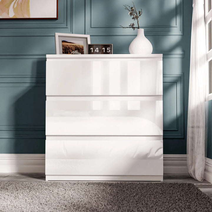 [White] high gloss 3 drawer chest front view against teal wall with clock and vase on surface