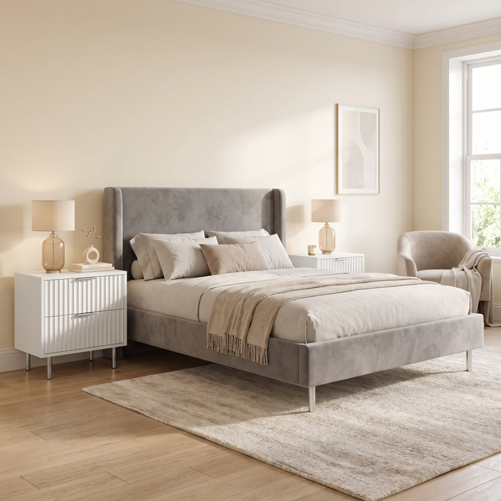 [White] Pair of White Fluted 2 Drawer Bedside Tables styled beside a grey upholstered bed.