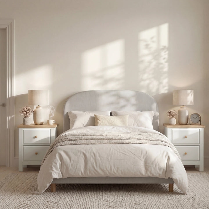 [White] Neatly made bed with white bedding and 2 bedside tables in both sides of the bed in a bright bedroom with natural light
