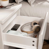 [White] close-up of open drawer in white bedside table showing phone headphones notebook and keys