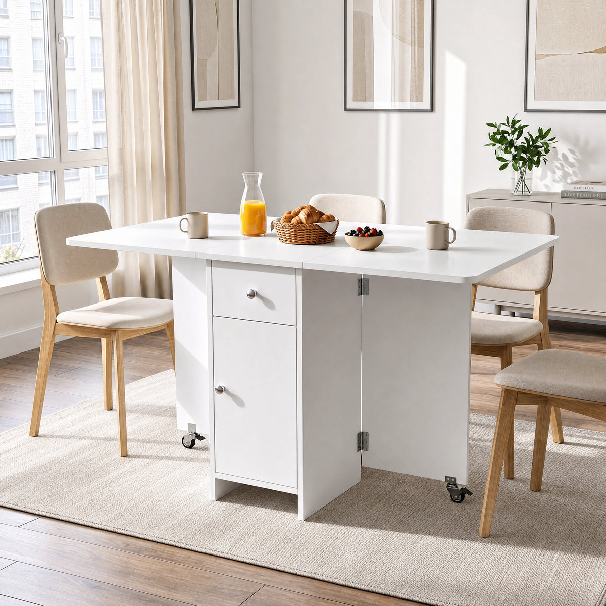 [White] Kitchen drop leaf table fully open and locked via caster supports styled with four chairs, orange juice and mugs.