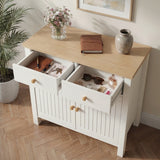 [White] sideboard with open drawers containing personal items, on a wooden floor with a plant and framed picture in the background