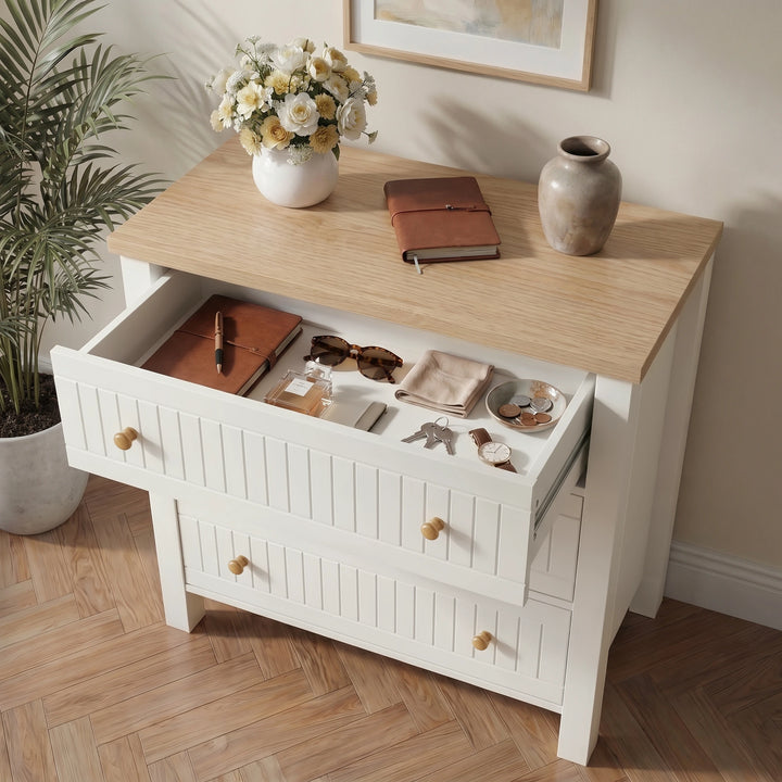 [White] chest of drawers with open drawer displaying items, on a wooden floor with a plant and framed picture in the background