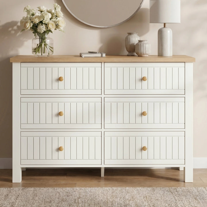 [White] Linra large 6 drawer chest front view against a beige wall room, oak top with lamp and stems