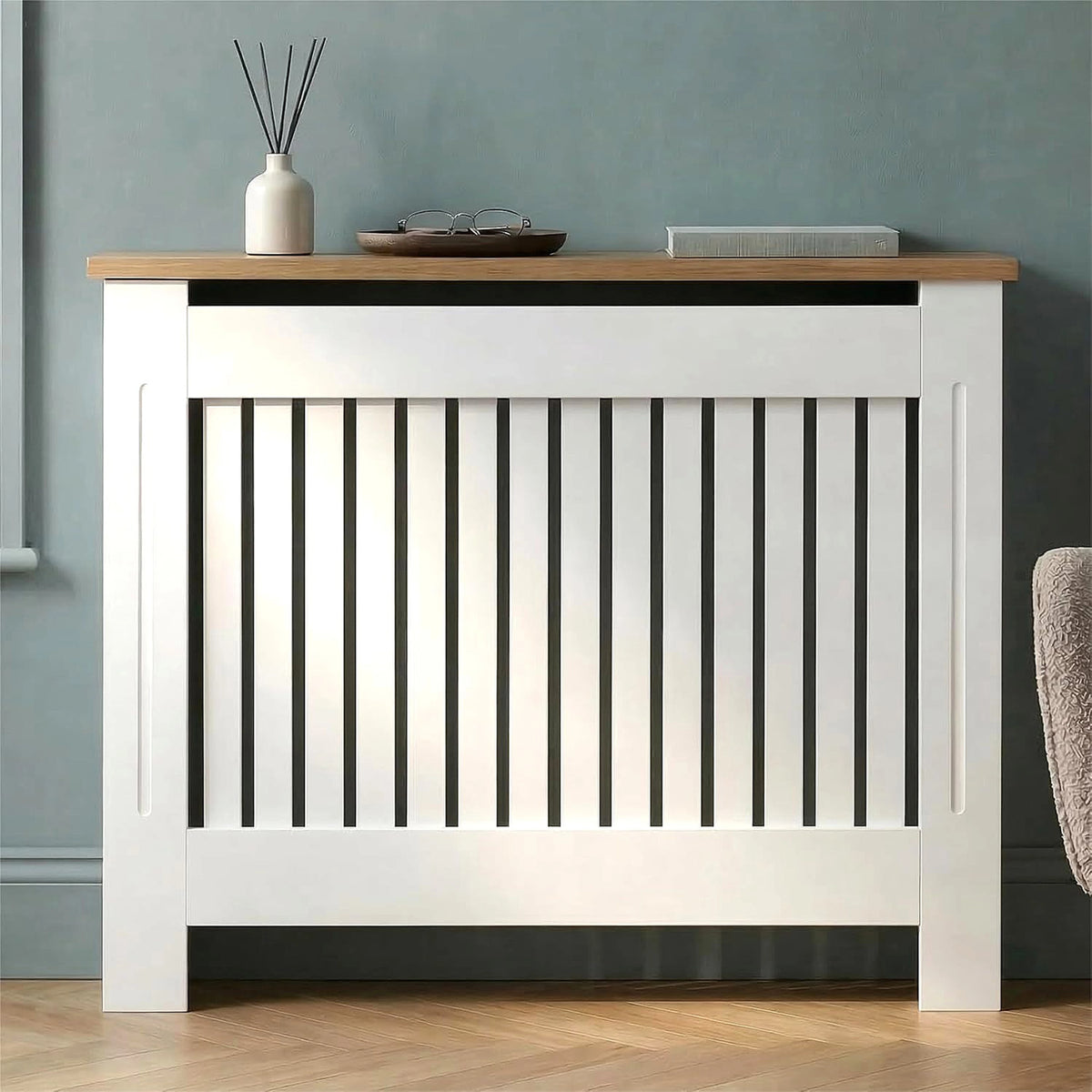 [Medium | White] Radiator Cover front view with oak top shelf holding a diffuser, tray, and book against a teal wall