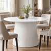 [White] round pedestal dining table in room with slatted pedestal base and beige chairs