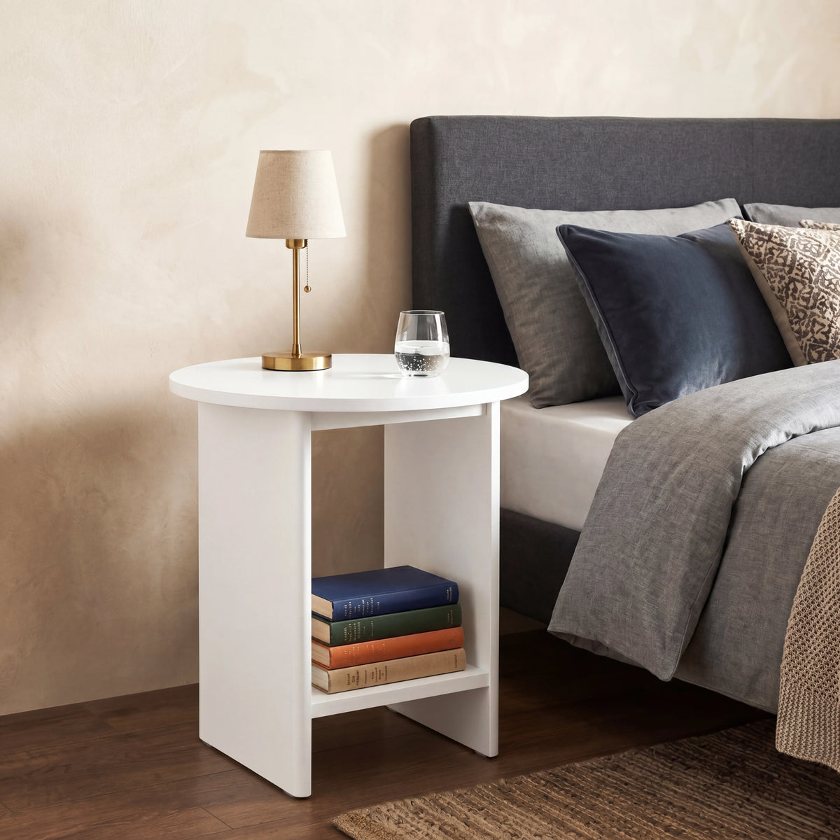 [White] Small Round Side Table with Shelf Living Room used as bedside table beside upholstered bed with brass lamp on top and stacked books on lower shelf
