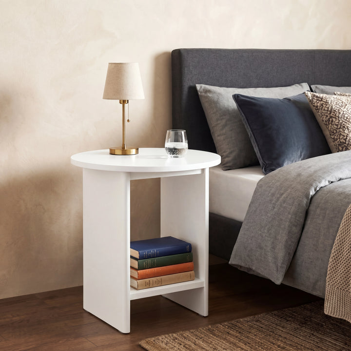 [White] Small Round Side Table with Shelf Living Room used as bedside table beside upholstered bed with brass lamp on top and stacked books on lower shelf