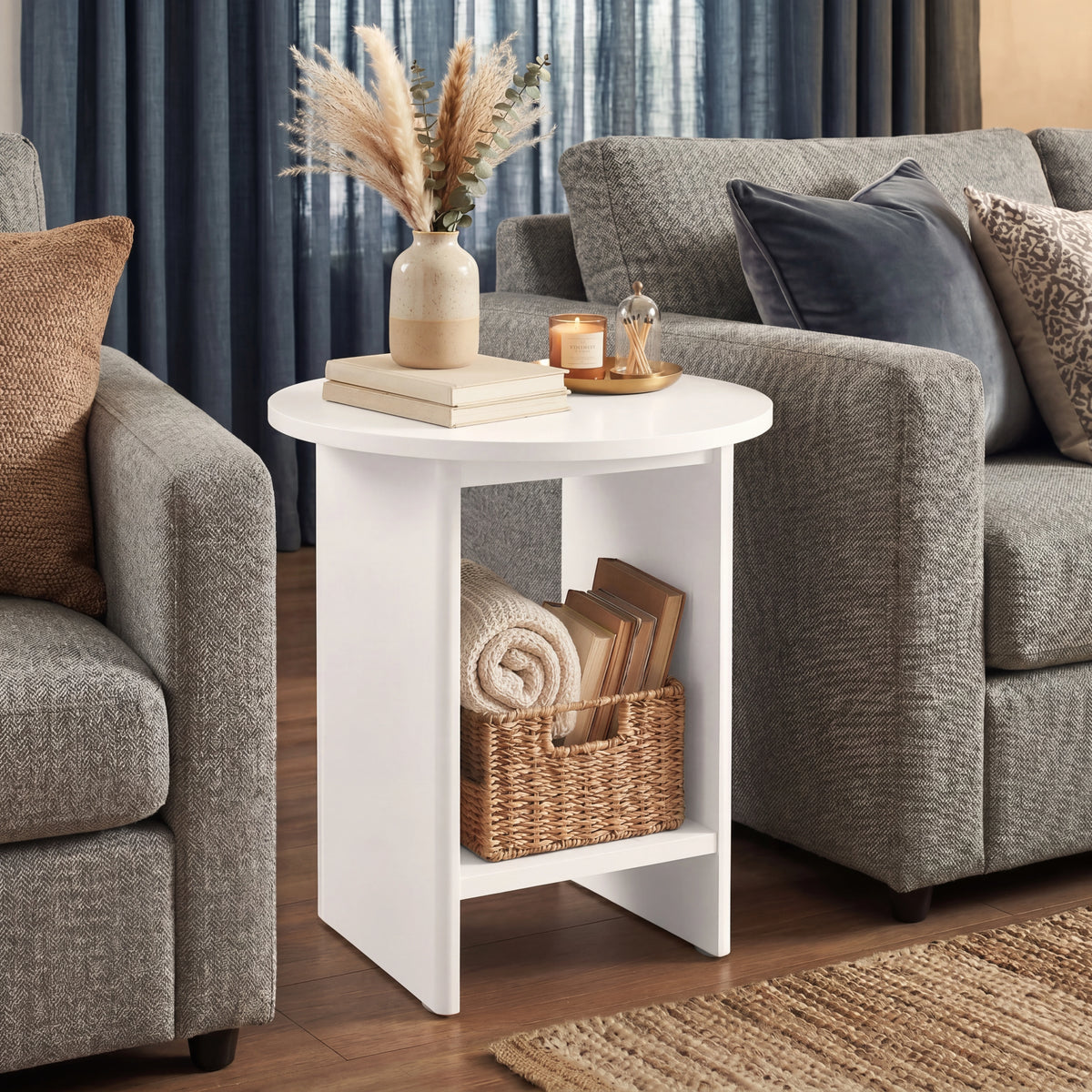 [White] Small Round Side Table with Shelf Living Room positioned between two grey sofas with botanical vase on top and wicker basket on lower shelf