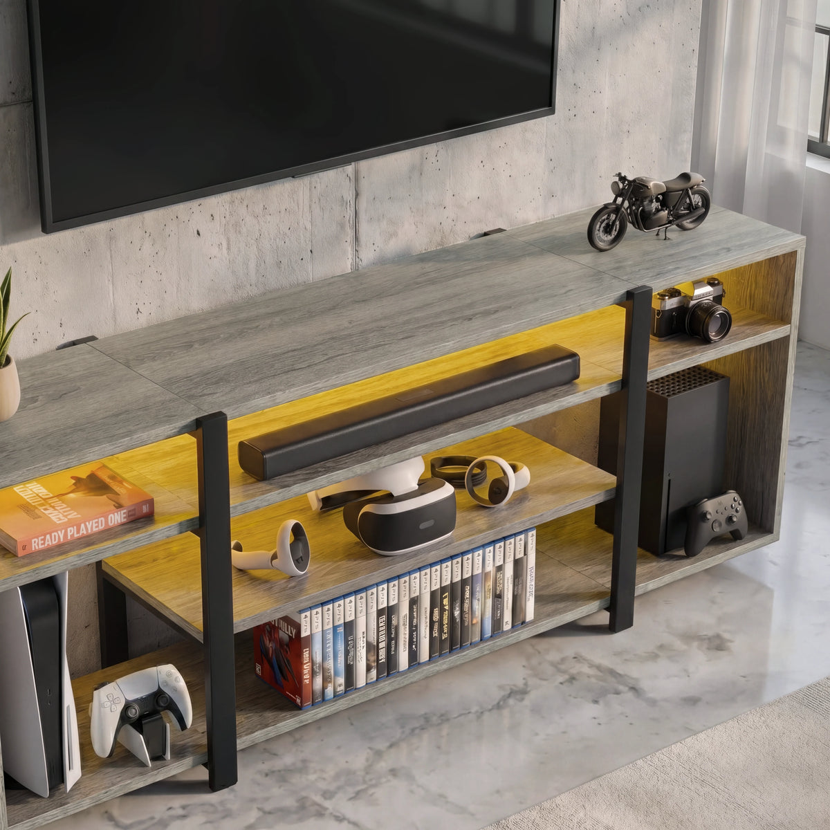 [Wooden Grey] Zelumi TV stand overhead close-up showing grey wood top surface, warm LED-lit shelves with VR headset, soundbar, console and game cases