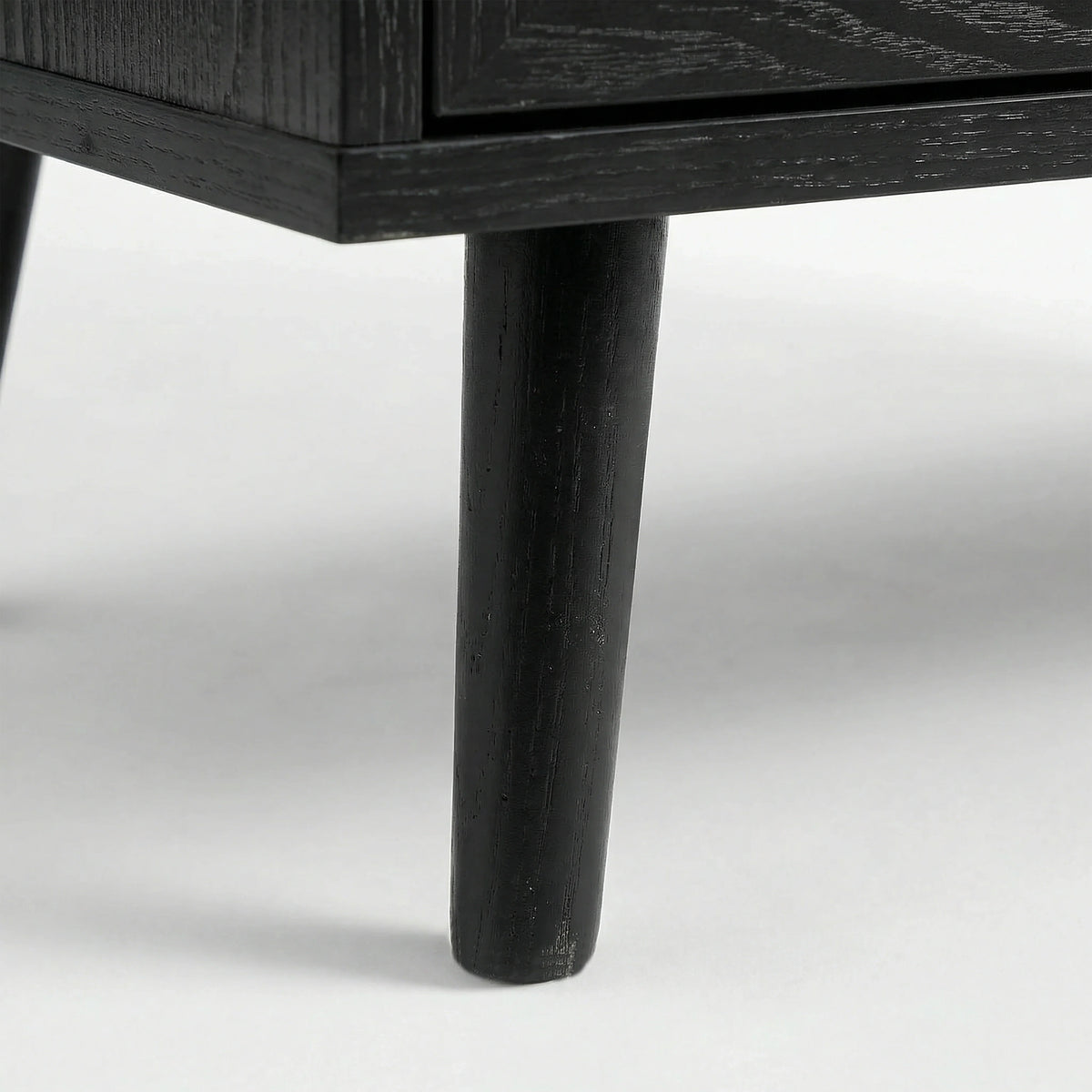 [Black] Detail of Wovena rattan bedside angled leg attached to cabinet, dark grain on leg and body